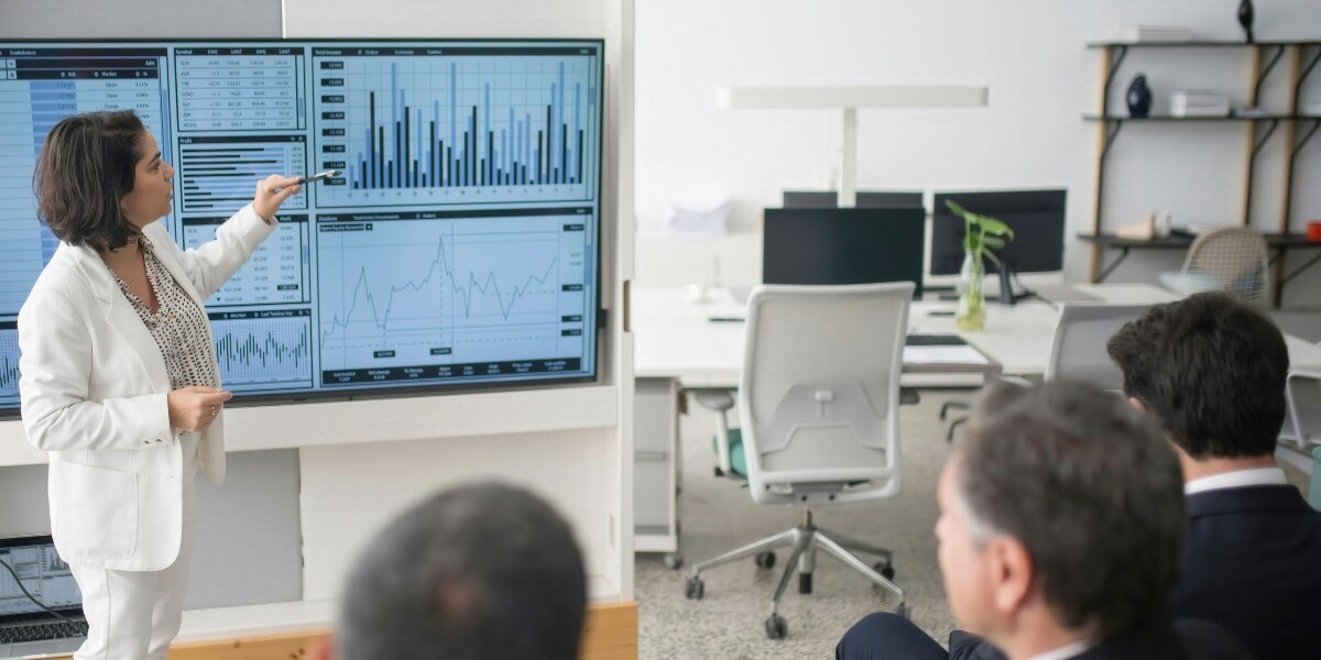 Businesswoman presenting SEO data and analytics on a large screen to a team in a modern office setting.