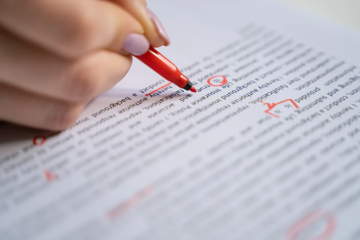Close-up of a hand marking corrections on a printed draft with a red pen