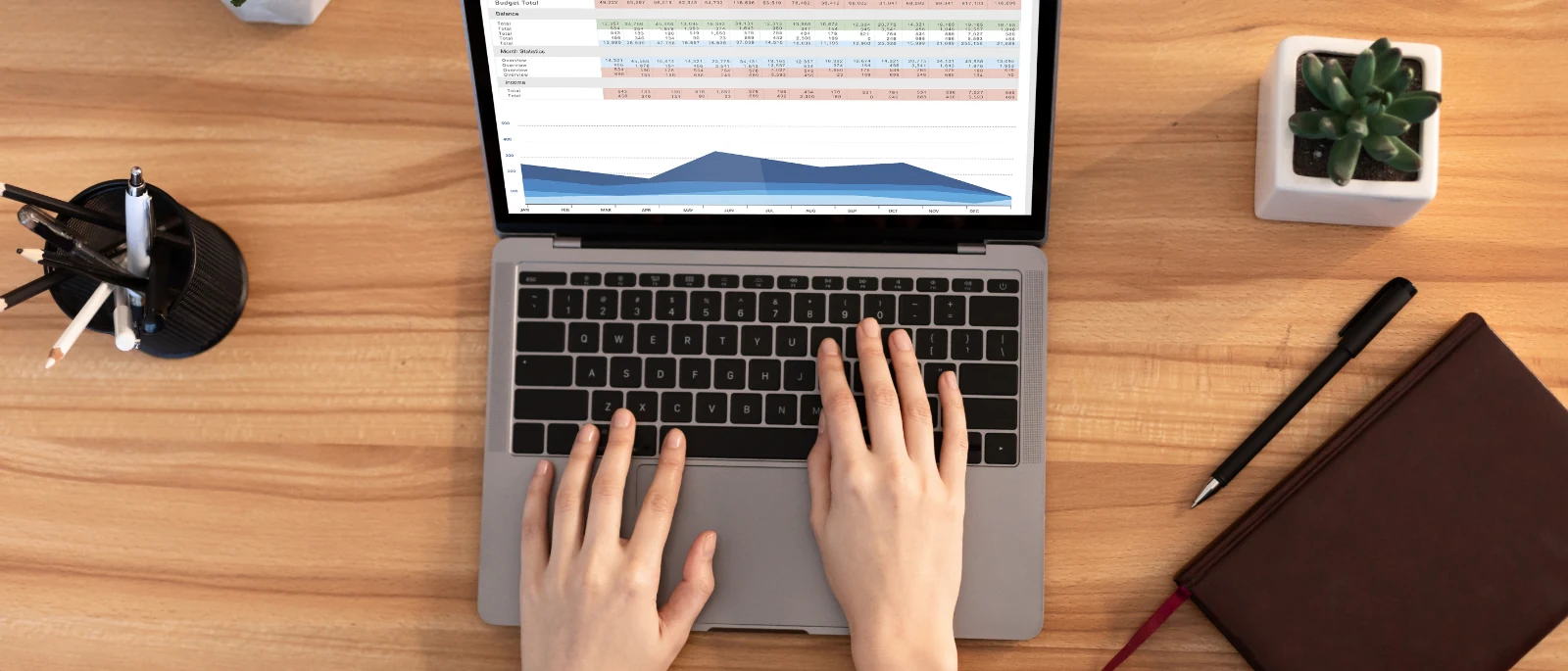 Overhead view of hands typing on a laptop showing a traffic report with a monthly area chart