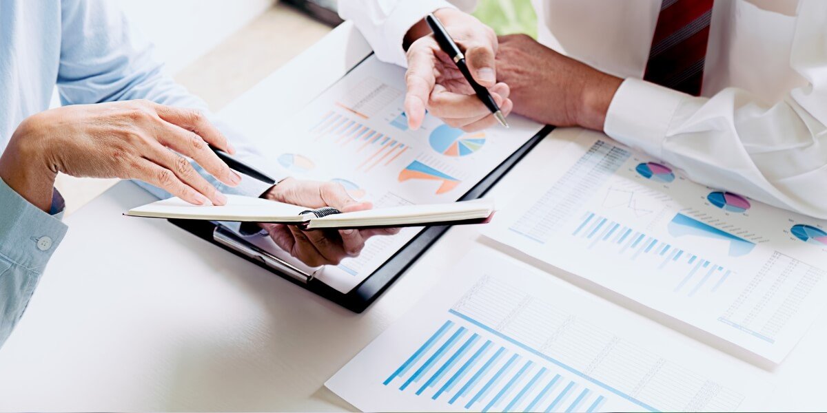 Two professionals analyzing SEO performance metrics and reports with charts and graphs, discussing data insights for business growth.